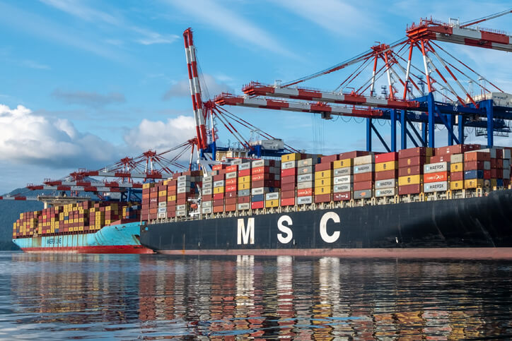 Barges on water with shipping containers and cranes on a sunny day.