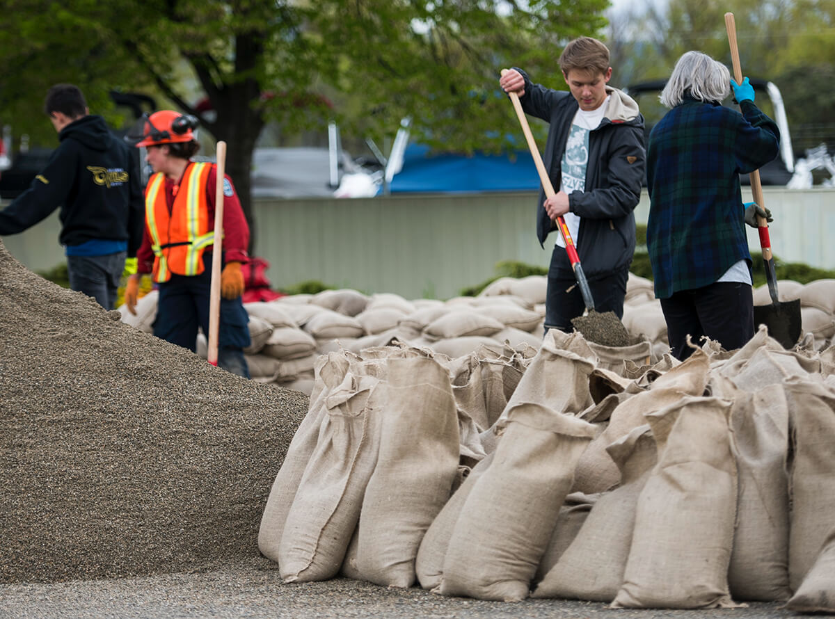 A group of people are seen working together to shovel sand into sandbags for flood protection.