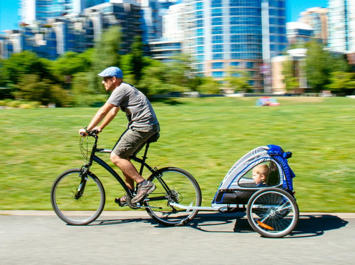 A white man on a bike cycles by with his child in an attached trailer.