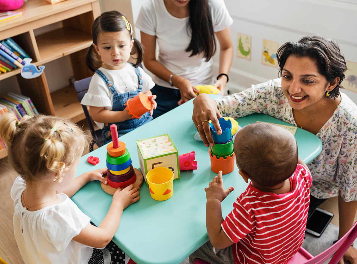 Two women play with toddlers in a childcare centre.
