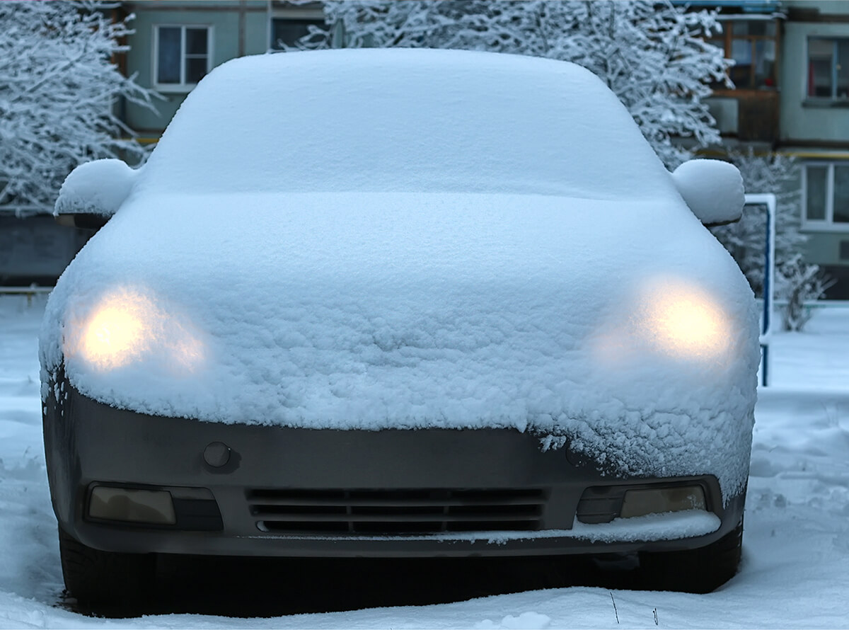 Front view of a car with headlights on and a sheet of snow covering the full the vehicle.