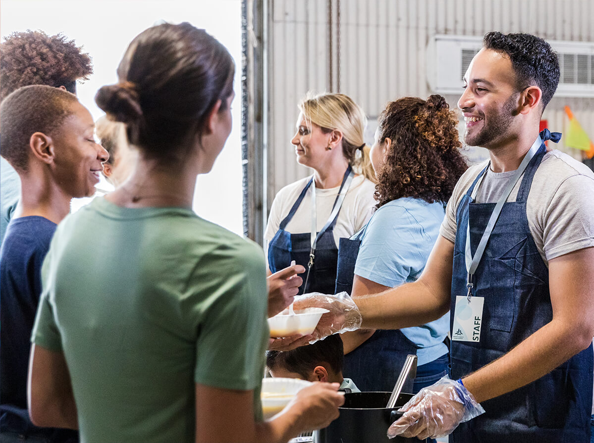 Smiling staff wearing aprons hand out food to a group of people.