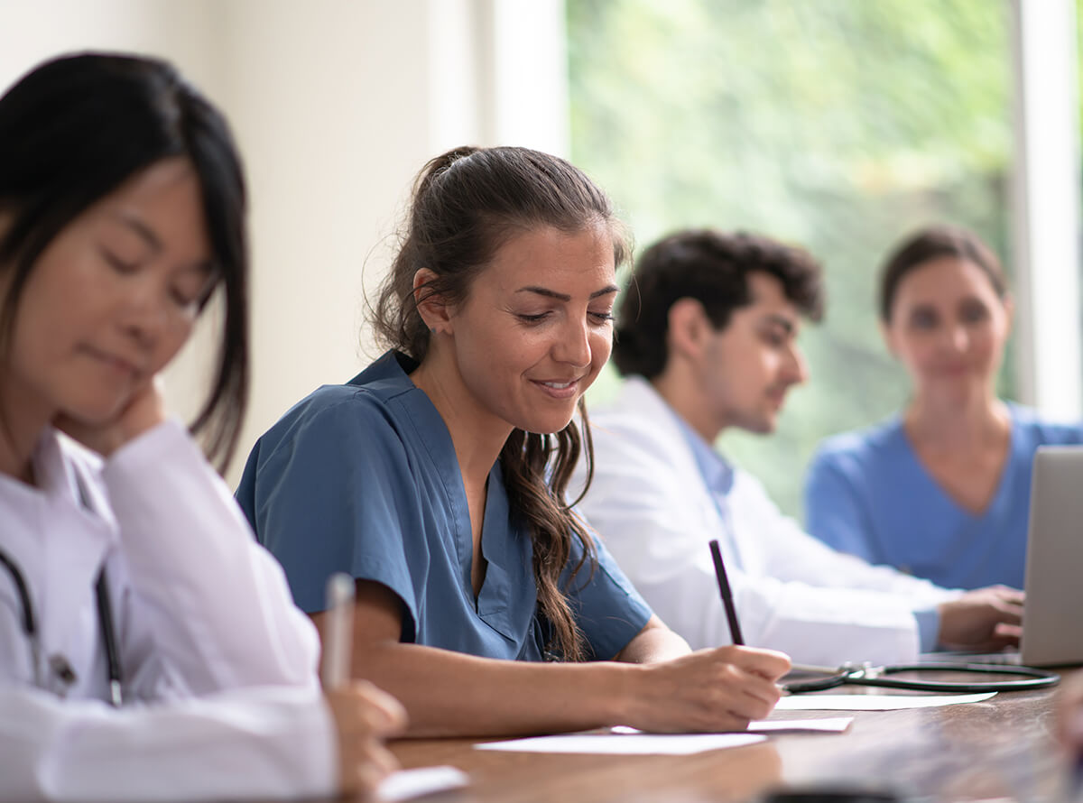 A group of medical students sit at a table writing and smiling.