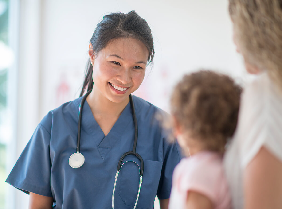 A doctor smiles at a young girl sitting with her mother.