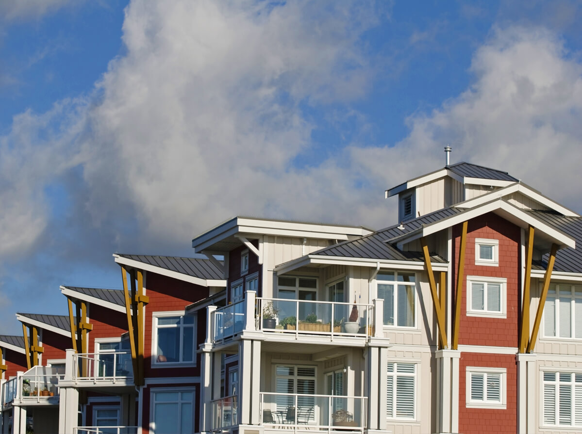 The top half of a residential building with pointed roofs. The building is red and cream coloured with patios, lots of windows, and light wood beams for reinforcement.