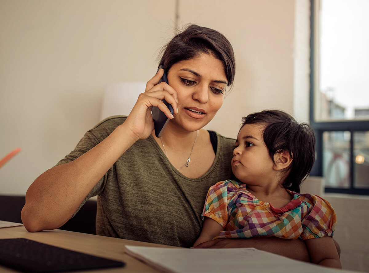 An Indian woman is on the phone sitting while holding her young daughter in her lap.