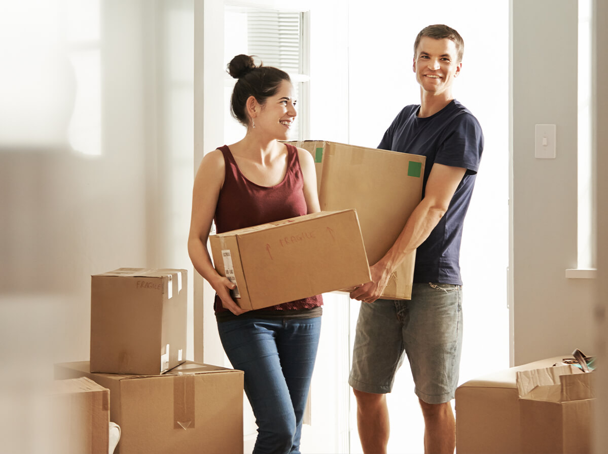 A young couple holds boxes as they move into a new place together.