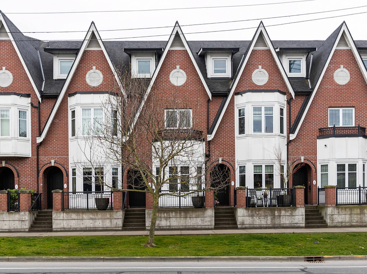 A row of tall brick townhouses with pointed roofs and white panelled bay windows on a grey day in Winter.