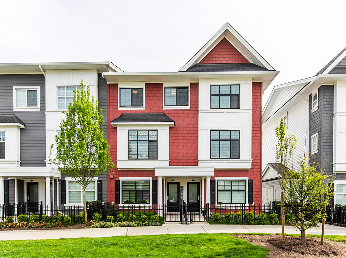 A red duplex between two grey duplexes on a residential street with freshly planted trees.