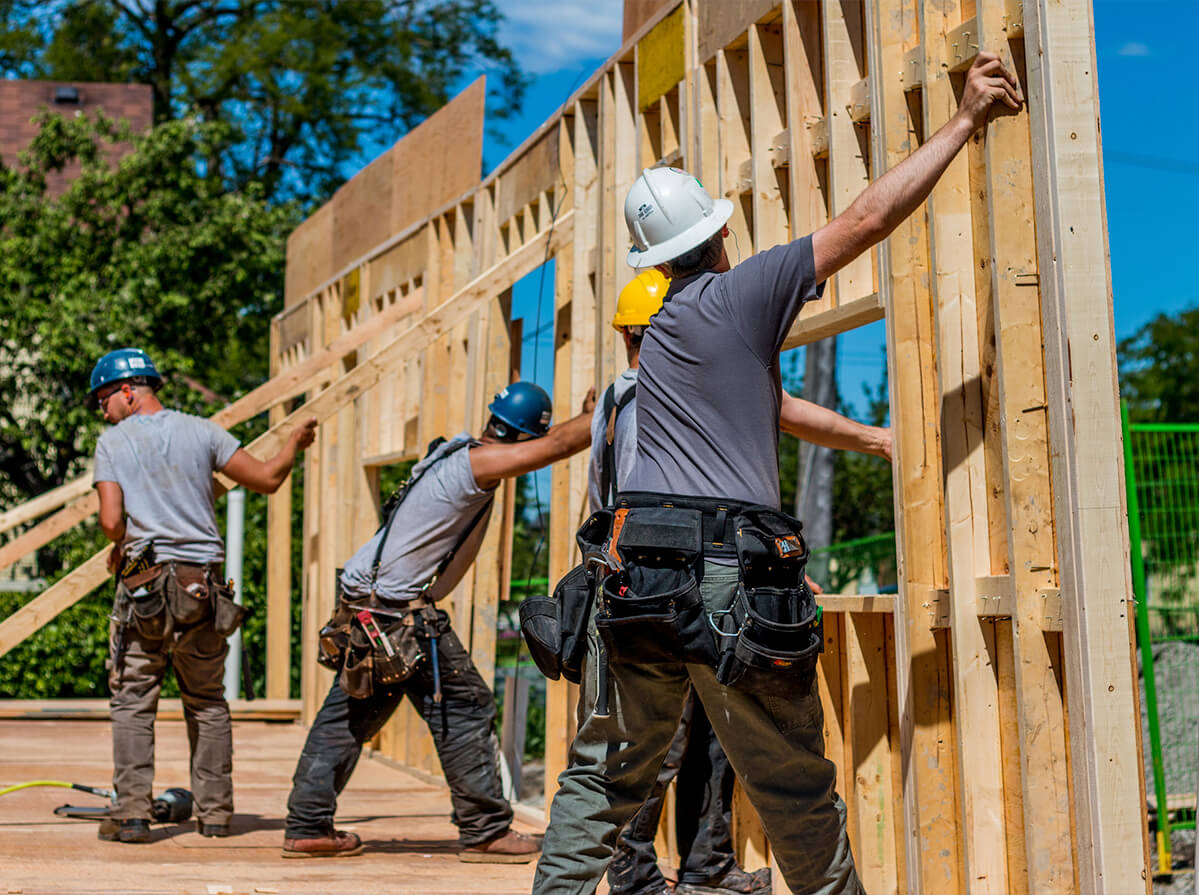 Construction workers on a sunny day raising a wall structure together.