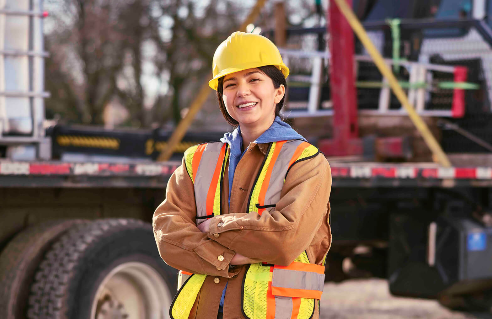 Worker wearing hard hat and hi-vis vest in front of large truck platform.