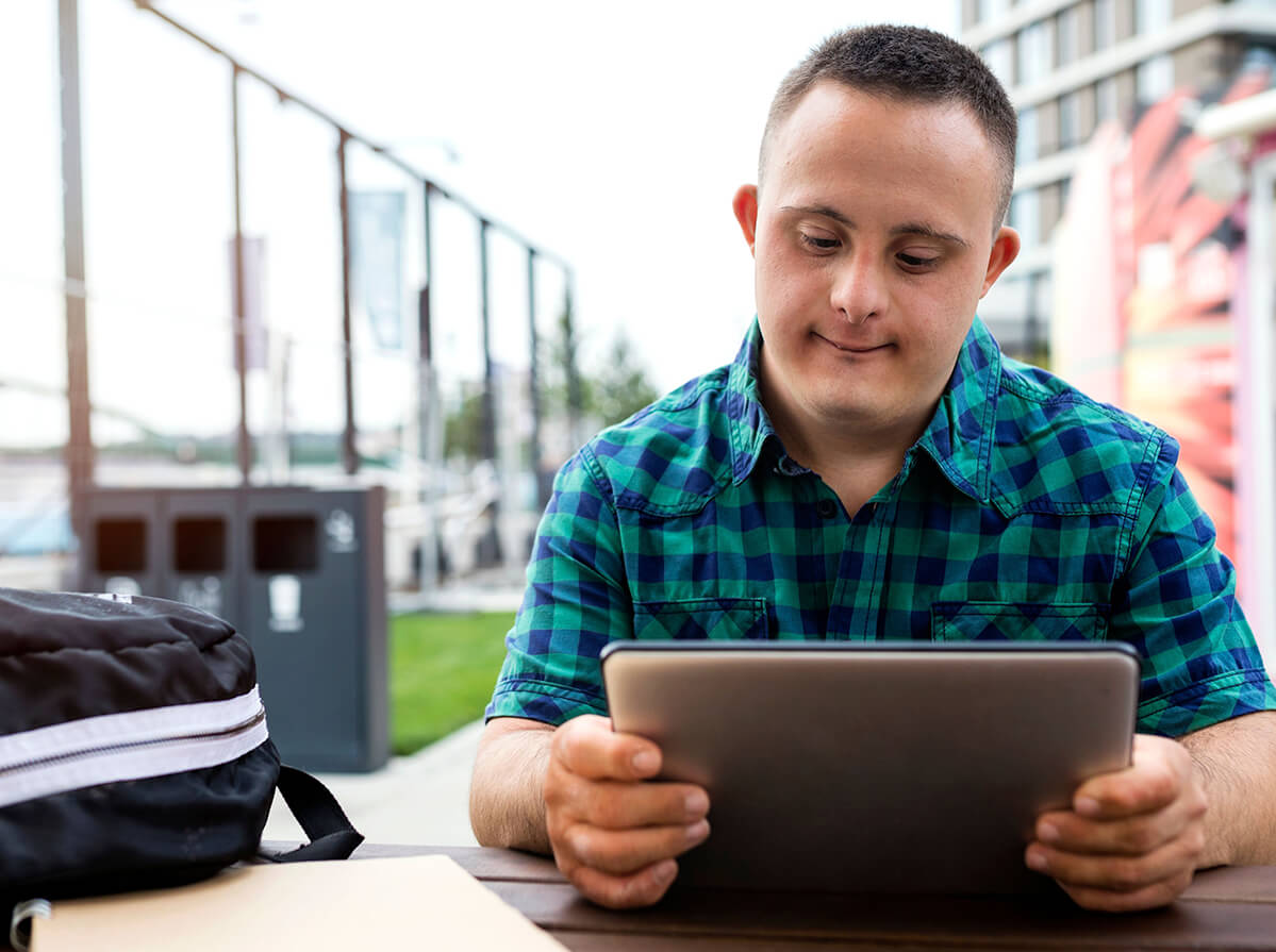 A young man reading from a tablet at an outdoor table.