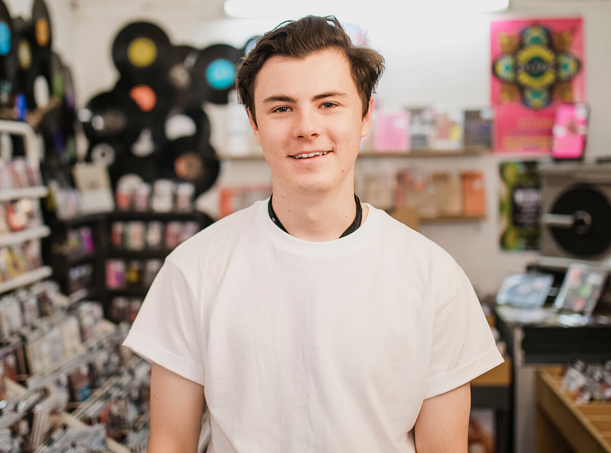 A young white person stands in a music media store and smiles at the camera.