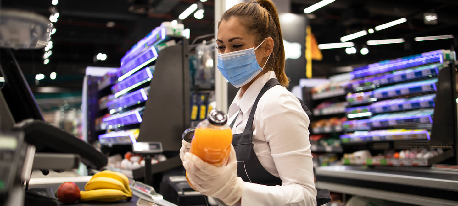 A woman wearing a mask and gloves works a cashier register at a grocery store.
