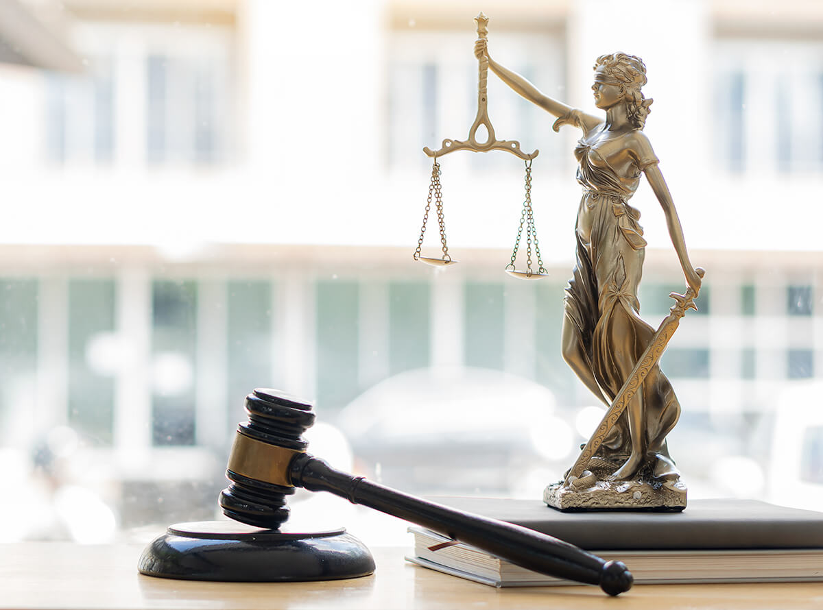 A small Lady Justice statue sits on two books in front of a window, next to a gavel.