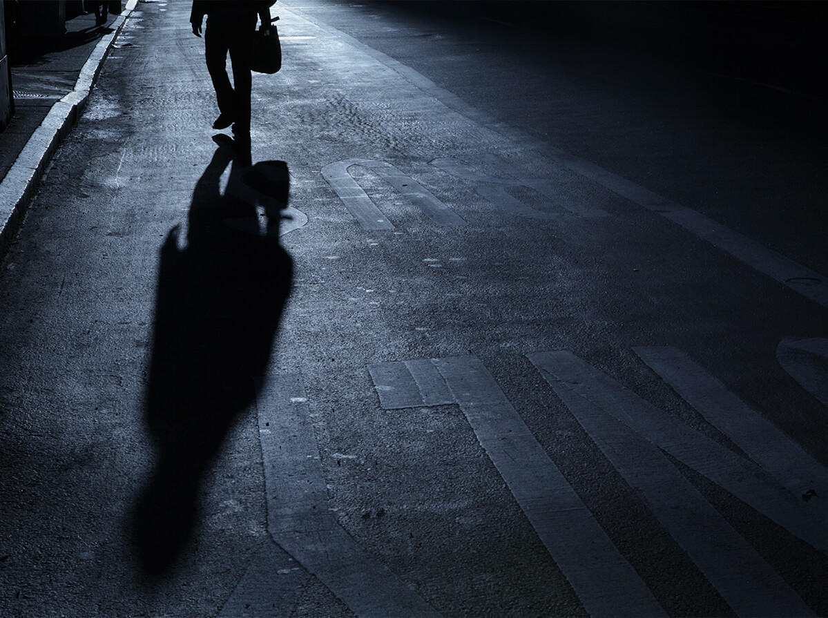 Dark photo of a person's shadow walking on a road at night.
